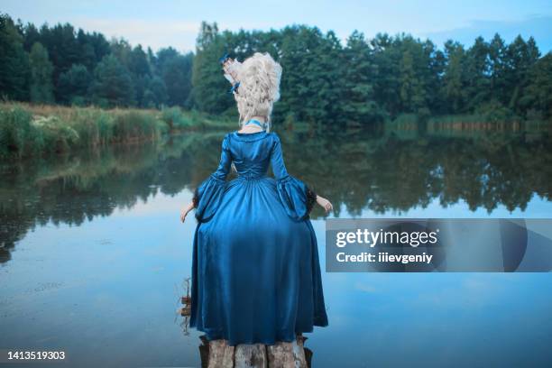 princesa renascentista com cabelo loiro no fundo do lago. maquiagem de beleza. rainha rococó de conto de fadas com navio em penteado sobre a natureza. modelo de vestido azul. mulher com estilo de cabelo histórico na ponte - countess - fotografias e filmes do acervo