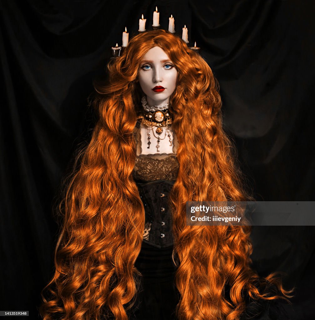 Mujer vampiro pelirroja. Cabello largo y rizado. Piel pálida. Vestido negro sobre fondo oscuro. Hermosa modelo con labios rojos. Outfit para halloween. Vampiro en corsé con peinado con velas en el pelo