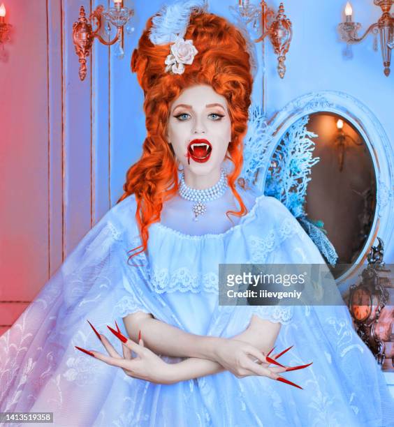 redhead vampire woman. long curly hair. pale skin. white dress on blue background. long claws. beautiful model with red lips. outfit for halloween. vampire with open mouth and fangs. blood on face - crazy white hair stock pictures, royalty-free photos & images