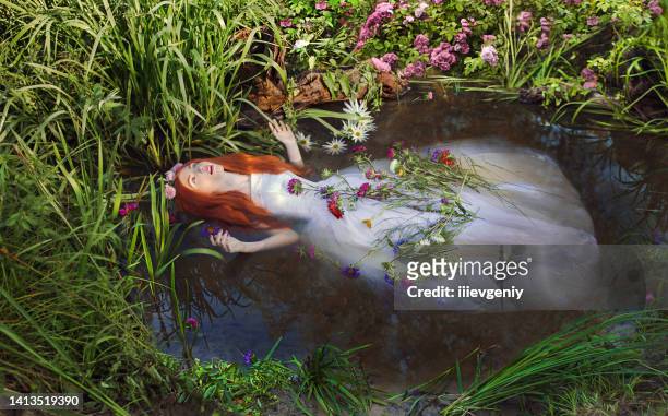 fairy redhead princess in white dress in stream. girl with long hair with flowers in pond. renaissance painting. ophelia. summer vegetation in nature - dead woman 個照片及圖片檔