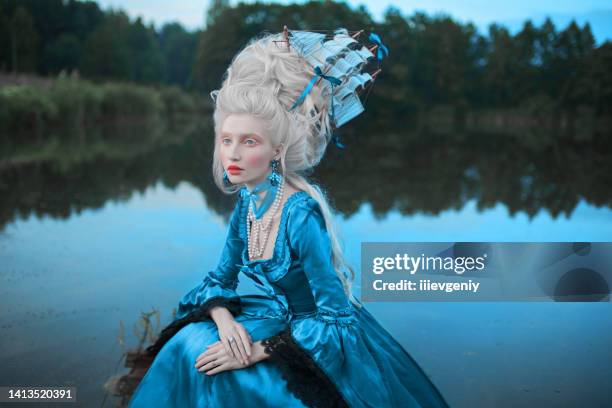 renaissance princess with blonde hair on lake background. beauty makeup. fairytale rococo queen with ship in hairstyle on nature. model in blue dress. woman with historical hair style on bridge - historische kleding stockfoto's en -beelden