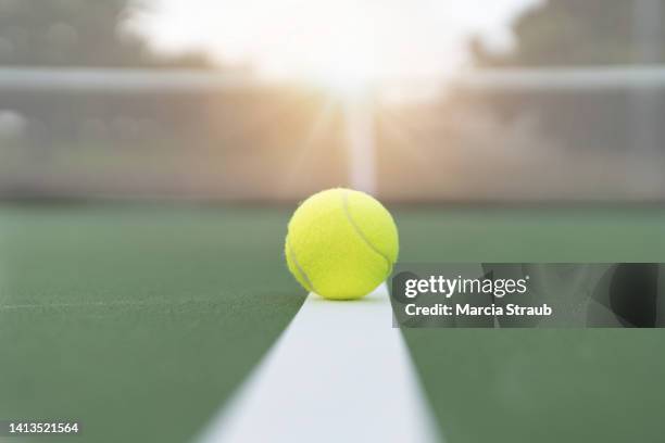 tennis ball on the white service line at sunset - tennisball stock-fotos und bilder
