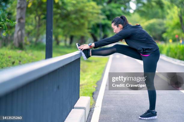 side view of  asian woman doing stretching exercise to warm up or a cooling down on a bridge railing at a public park outdoors. - runner warming up stock pictures, royalty-free photos & images