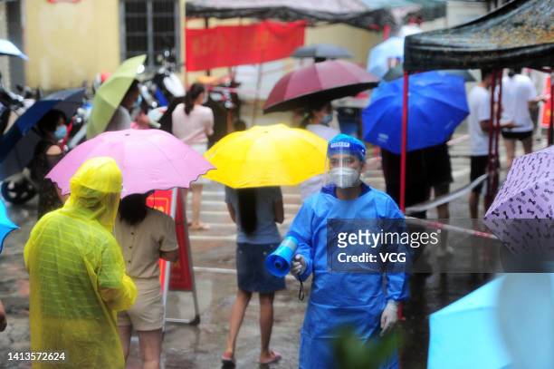 Medical worker holding a megaphone keeps order as residents queue up in rain for COVID-19 nucleic acid tests on August 8, 2022 in Sanya, Hainan...