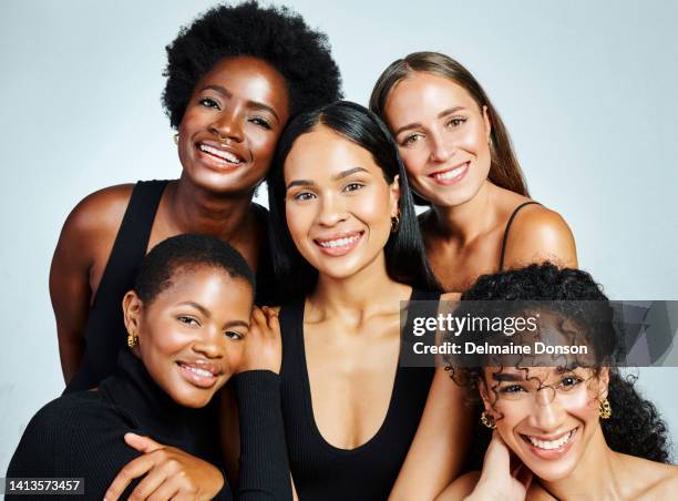 gruppo di donne diverse e felici che mostrano bellezza, cura della pelle e cosmetici mentre posano insieme su uno sfondo grigio dello studio. ritratto femminile internazionale di donne emancipate con sorrisi luminosi - black woman happy white background foto e immagini stock