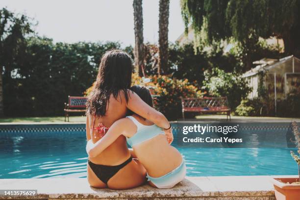 rear image of teenager girls sitting at poolside embrancing - drinkwater kante stock-fotos und bilder