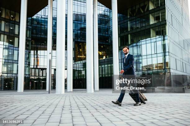 businessman in full suit near modern office building or airport, with suitcase and sunglasses - hungary hotel stock pictures, royalty-free photos & images