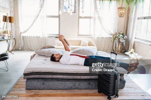 businessman arriving to hotel, sitting or lying on bed and using smart phone for cryptocurrency trading - hungary hotel stock pictures, royalty-free photos & images