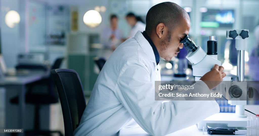 Research scientist analyzing a sample, looking into a microscope, conducting an experiment. Male biologist or chemist working on a futuristic medical development in a laboratory.