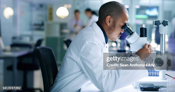 research scientist analyzing a sample, looking into a microscope, conducting an experiment. male biologist or chemist working on a futuristic medical development in a laboratory. - life science stock pictures, royalty-free photos & images