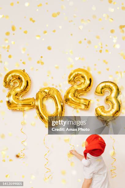 happy kid are enjoying confetti near white wall with gold christmas balloons. celebrating new year 2023. christmas concept - new year's eve children stock pictures, royalty-free photos & images