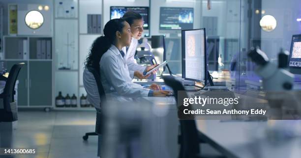 científicos médicos serios y enfocados que analizan escaneos de investigación en una computadora, trabajando hasta tarde en el laboratorio. los trabajadores de laboratorio examinan y hablan sobre los resultados de un chequeo mientras trabajan horas extr - science fotografías e imágenes de stock