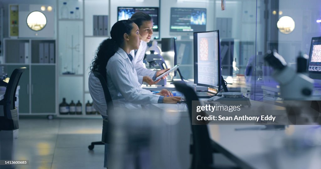 Cientistas médicos sérios, focados, analisando pesquisas em um computador, trabalhando até tarde no laboratório. Os funcionários do laboratório examinam e falam sobre os resultados de um check-up enquanto trabalham horas extras