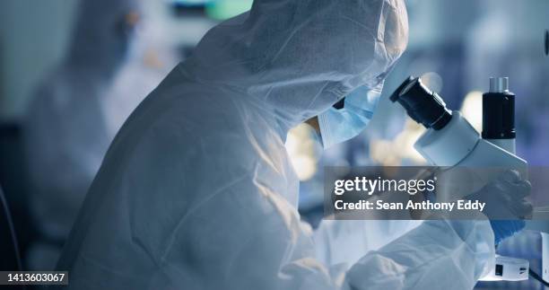 scientist, chemist or engineer analysing the cure for covid in a laboratory using a microscope. researching a virus and finding a cure through science and innovation during a pandemic - roupa protetora imagens e fotografias de stock