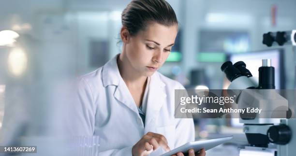 serious female scientist recording virus cell data onto online database with a tablet while working inside a lab or research center. focused researcher reading medical journal in a health care center - woman scientist bildbanksfoton och bilder