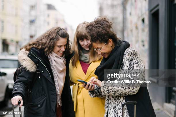 three women looking at smartphone while visiting new city - travel stock-fotos und bilder