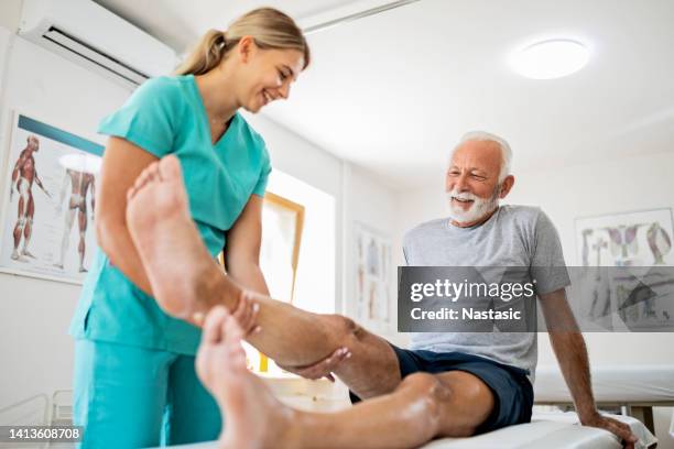 young smiling physiotherapist working with a senior male patient - medische procedure stockfoto's en -beelden
