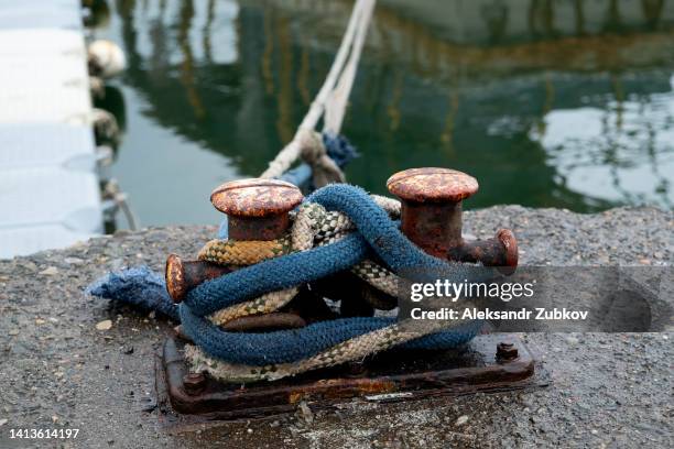 a ship's bollard with mooring ropes attached, mounted on a concrete berth by the ocean. mooring cable tied with a sea knot, on the shore near the azure sea. - être ancré photos et images de collection