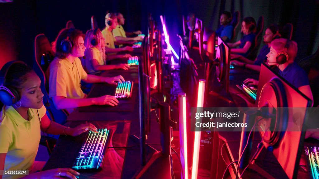 Diverso equipo femenino de jugadores profesionales amarillos con líder de etnia africana que compite en el campeonato de eSport de videojuegos. Equipo azul en el otro lado