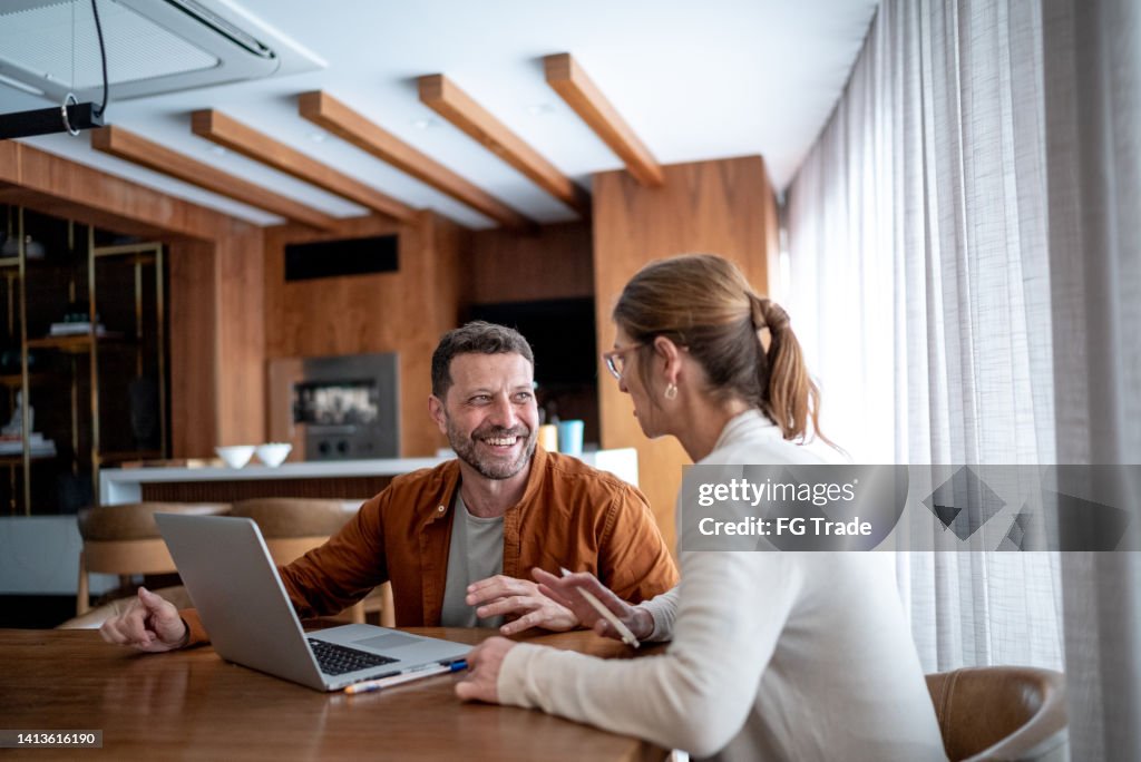 Couple d’âge mûr parlant et utilisant l’ordinateur portable à la maison