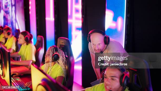 diverse yellow pro gamer team with a coach and african ethnicity players competing in video game esport championship - esports stock pictures, royalty-free photos & images