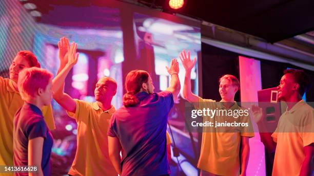 diverse yellow pro gamer team with african ethnicity players winning video game esport championship. celebrating with blue team, high fives - winners podium people stock pictures, royalty-free photos & images