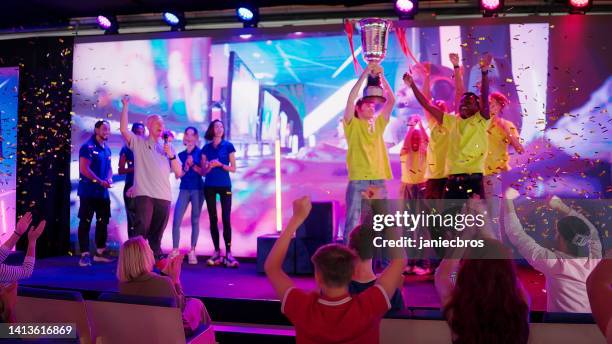 diverse yellow pro gamer team with african ethnicity players winning video game esport championship. raising trophy - awards broadcast stock pictures, royalty-free photos & images