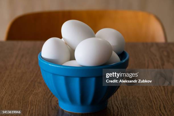 raw or boiled white eggs in a shell, in a plate on a wooden kitchen table. eggs for cooking, baking and for making omelets. animal protein. the concept of a healthy balanced diet. preparation for the easter holiday. eggs for painting. - blue bowl stockfoto's en -beelden