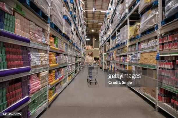 young woman pushing empty trolley down aisle of wholesaler - shopping trolley photos et images de collection