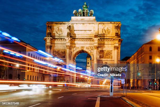 puerta de la victoria en múnich con líneas de luz borrosas de tráfico a la hora azul - múnich fotografías e imágenes de stock