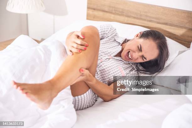 a strong cramp in the calf of a young woman lying on the bed in the bedroom. - bein stock-fotos und bilder