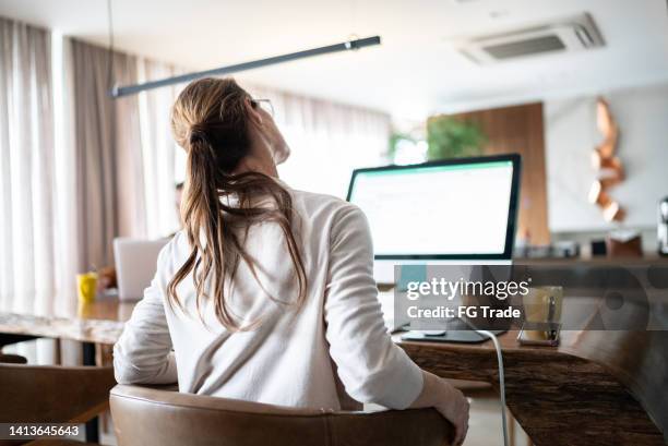 mature woman stretching with back pain while using the computer at home - cervical vertebrae stock pictures, royalty-free photos & images