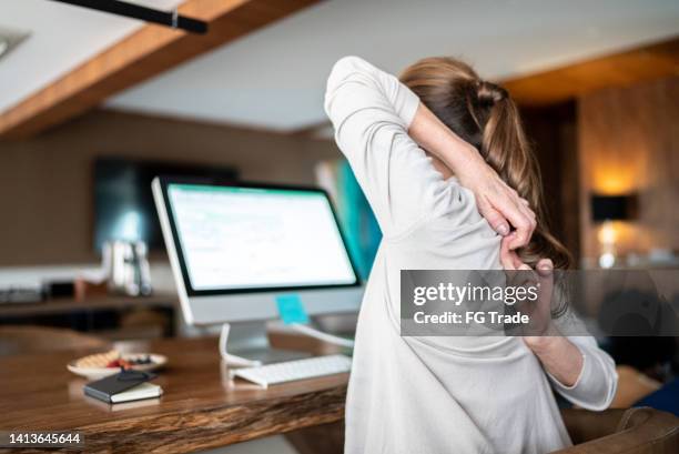 mature woman stretching in the chair while using the computer at home - ergonomie stockfoto's en -beelden