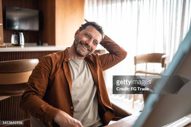 mature man stretching while watching tutorial in the computer at home - home office ergonomics stock pictures, royalty-free photos & images