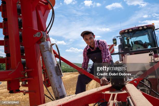 ein traktorfahrer arbeitet an der angeschlossenen ausrüstung seines traktors. - bartstoppel stock-fotos und bilder