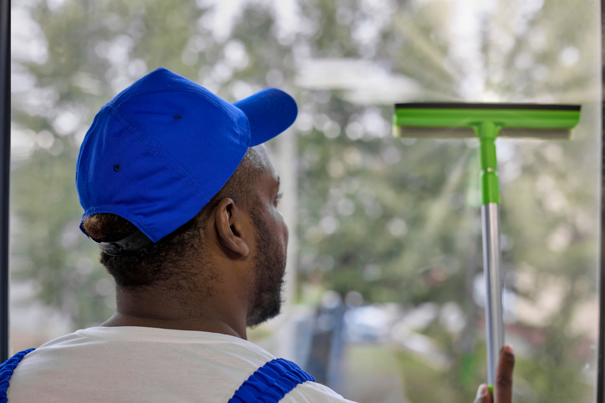 Strong African-American man in white T-shirt and cap with window cleaning brush Strong African-American man in white T-shirt and cap with window cleaning brush