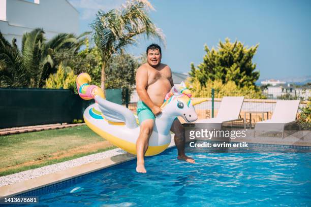 fat man jumping to pool with inflatable unicorn - man on float stock pictures, royalty-free photos & images