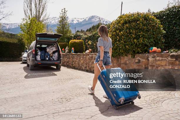 a young woman pulling a suitcase to a car leaving a rural hostel finishing summer holidays. travel concept - taxi españa stockfoto's en -beelden