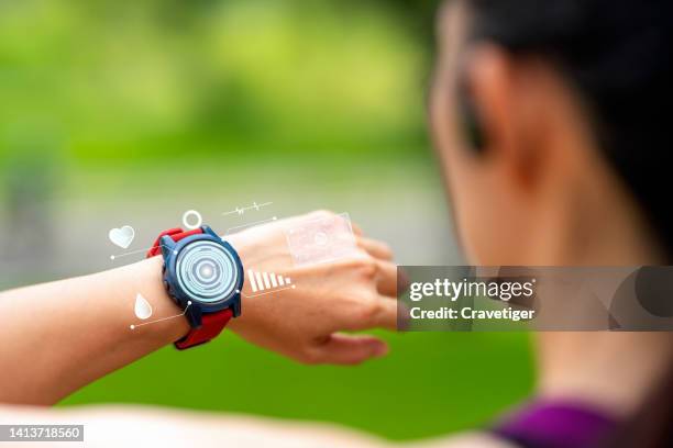 rear view of female with digitization display. asian female use the smartwatch for check the heart rate and health information on her smartwatch with digitization that synchronization with earphones after jogging in a public park. - fitness tracker stock pictures, royalty-free photos & images