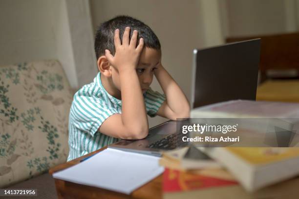 asian kid showing confused expression in front of laptop - illiteracy stock pictures, royalty-free photos & images