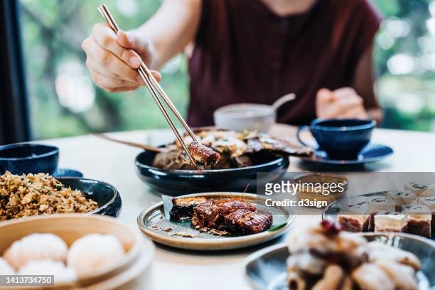 cropped shot of young asian woman enjoying assorted freshly served delicate dim sum and dishes with chopsticks in a chinese restaurant. traditional chinese culture. yumcha. eating out lifestyle - dim sum stock-fotos und bilder