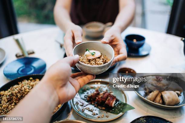 personal perspective of asian couple enjoying assorted dim sum and delicate dishes in chinese restaurant together. woman is serving a bowl of fried rice across the table to man. traditional chinese culture and food culture. yumcha. eating out lifestyle - fried rice stock-fotos und bilder