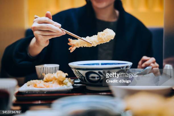 Cropped shot, mid-section of young Asian woman dining in a Japanese restaurant, enjoying delicate freshly served Japanese cuisine, seafood tempura on the dining table. Asian cuisine and food culture. Eating out lifestyle