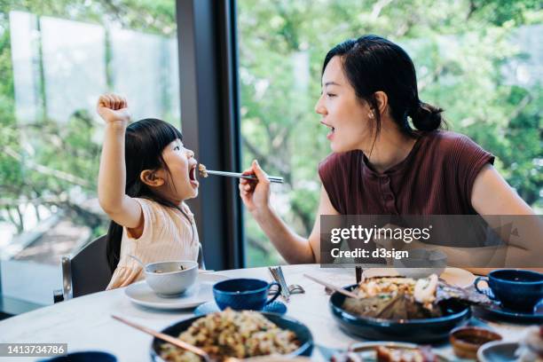 joyful young asian mother and little daughter enjoying assorted traditional chinese dim sum and dishes in a chinese restaurant. asian family enjoying a happy meal together. family and eating out lifestyle - chinese culture stock-fotos und bilder