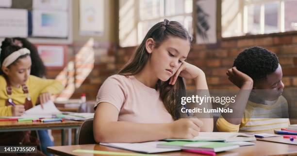 study, classroom and education for children learning and writing an essay or exam at school. bored and serious teenage student girl using notebook during a test or educational lesson in diverse class - 12 13 girl closeup stock pictures, royalty-free photos & images