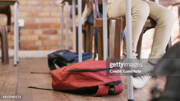 beine von kindern, die in einer klasse in einer grundschule sitzen und lernen und eine qualitativ hochwertige ausbildung erhalten. schüler, die in einem klassenzimmer mit ihren rucksäcken oder taschen auf dem boden lernen - small child sitting on floor stock-fotos und bilder