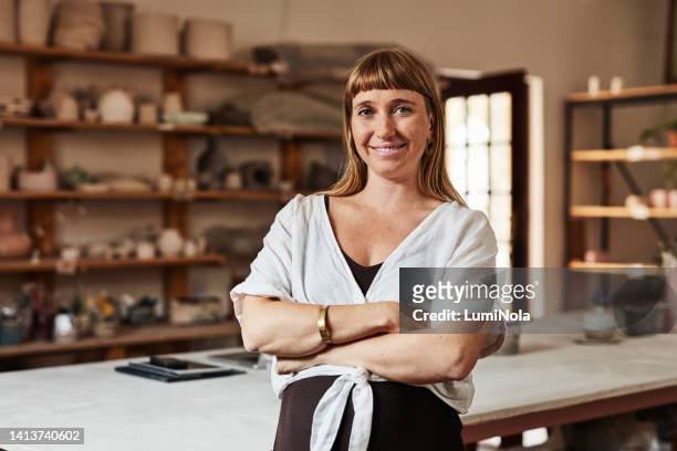 smiling, proud and confident portrait of a mature businesswoman with arms crossed standing in creative art studio. casual female worker inside modern ceramic design workspace. - artist portrait stock pictures, royalty-free photos & images