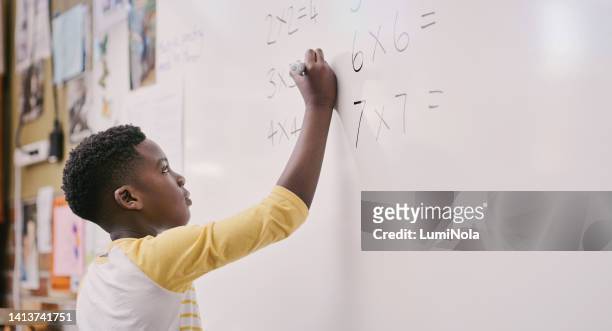 bildung, klassenzimmer und lernen, während schwarze schüler eine mathematische gleichung lösen und antworten auf das whiteboard schreiben. kluger kleiner schuljunge, der eine multiplikationssumme macht und eine lösung im unterricht berechnet - mathematik stock-fotos und bilder