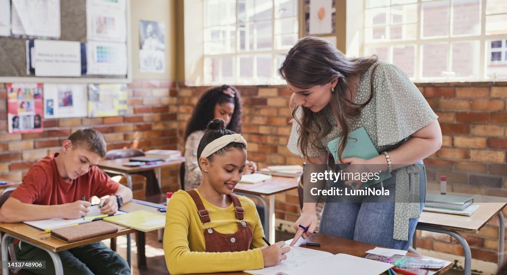 Teacher helping, teaching and assisting school students with education inside a creative classroom. Young children busy, learning and concentrating in class with a female educator during a lesson