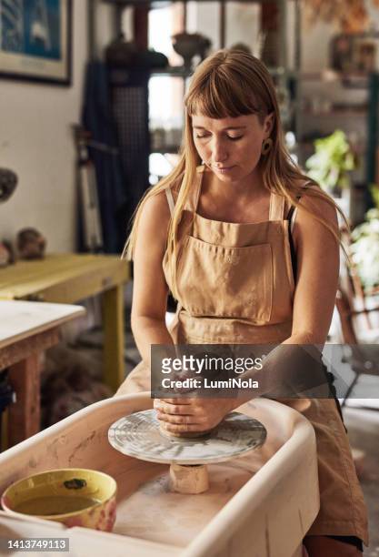 creative, art and female relaxing in her home studio and enjoying her hobby of pottery making handmade clay crafts. young artistic woman working on a potter's wheel while sitting in her workshop - art manke stock pictures, royalty-free photos & images